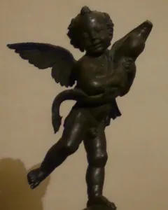 Bronze putto with a dolphin, the winged child poised on one foot atop a small base.