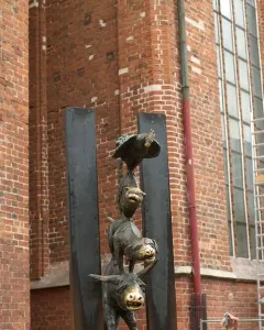 Bronze Bremer Stadtmusikanten sculpture with a donkey, dog, cat, and rooster stacked in a tower against a brick wall.