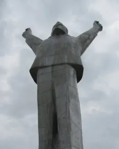 Monument to Stjepan Filipović seen from below, with the figure raising both arms against a cloudy sky.