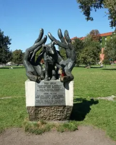 Bronze Monument to Dog Jock sculpture showing a dog nestled between two large hands on a stone pedestal in a park.