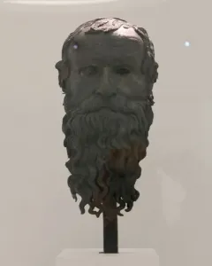 The Porticello Head bronze sculpture of an older man with a wavy beard and hollow eyes on a pedestal.