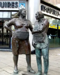 Monument to the Unknown Woman Worker, with two bronze women statues on a sidewalk beside a modern building.