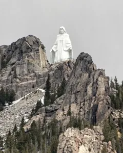 Our Lady of the Rockies statue standing on a rocky mountain peak with outstretched arms.