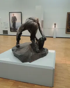 Cobblestone, a dark bronze headless figure crouching and holding a large stone.