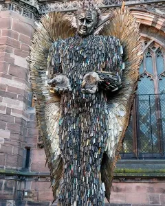 Knife Angel sculpture with outstretched hands and feathered wings outside a stone cathedral.