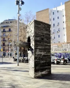 Monument to Narcís Monturiol, a tall textured concrete block with a submarine-like metal model protruding from its side, on a city sidewalk.