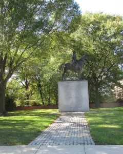 Bernardo de Gálvez equestrian statue on a tall stone pedestal surrounded by trees.