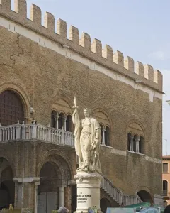 Monumento dell\'Indipendenza statue of a draped female figure holding a spear in front of a historic brick building.