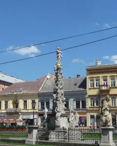 Marian Column with a haloed statue of the Virgin Mary, surrounded by figures and a metal fence.
