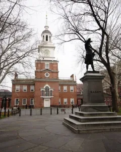 Commodore John Barry statue on a stepped stone pedestal in front of a historic brick building with a clock tower.