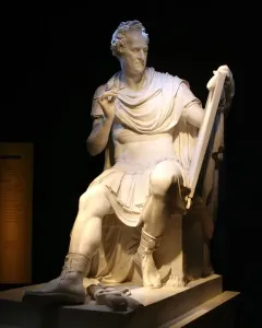 Seated George Washington sculpture in white stone, holding a stylus and tablet, with an information panel beside it.