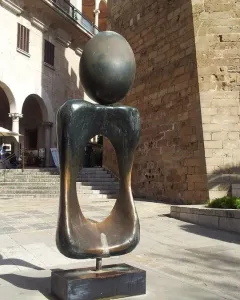 Monument a la dona bronze sculpture with a dark oval sphere balanced on an abstract hollow form outdoors.