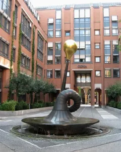 Erich-Schulze-Brunnen, a dark metal fountain with a curved trumpet-like form topped by a gold sphere in a paved courtyard.