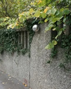 A polished spherical sculpture mounted on a textured concrete wall with ivy and a metal plaque below.