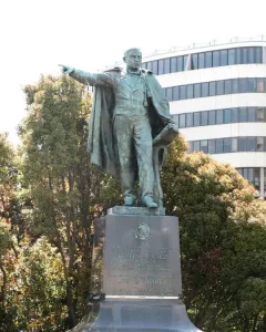 Bronze statue of Benito Juarez standing on a multi-tiered stone pedestal, holding papers and pointing forward.