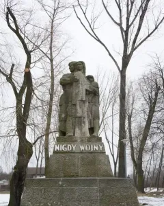 War Never Again stone monument showing a man embracing a woman and child on a tiered base inscribed “NIGDY WOJNY.”