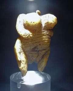 Venus of Hohle Fels figurine with pronounced breasts, rounded abdomen, and a loop-like top against a dark background.