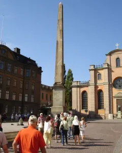 The Obelisk at Slottsbacken rises from a cobblestone plaza with people gathered around it.