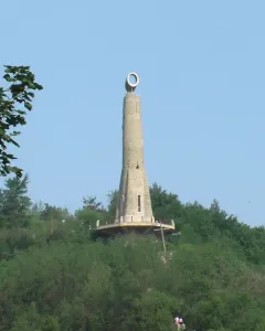 The Thanksgiving Candle monument rises from a wooded hill under a clear blue sky.