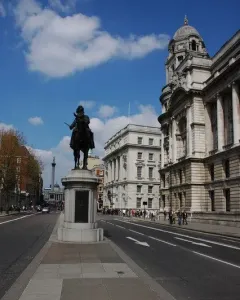The Duke of Cambridge equestrian statue silhouetted against a grand stone building and blue sky.