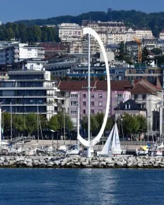 Éole, a large white curved sculpture on a rocky breakwater beside sailboats in a marina.