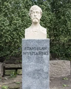 Stanisław Wyspiański bust on a speckled stone pedestal in a wooded outdoor setting
