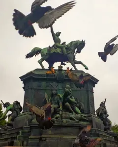 Dom Pedro I Equestrian Statue on a sculpted pedestal, with pigeons flying around it and ornate lampposts nearby.