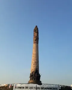 The Roundabout of the Disappeared monument with a tall stone column, statues at the top and base, and a banner reading \