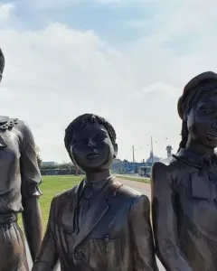 Kindertransport bronze sculpture of three children standing outdoors near a road and grassy area.