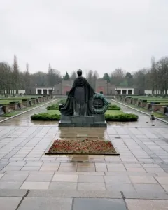 The Soviet War Memorial Schönholzer Heide statue seen from behind, holding a wreath over a wet paved plaza.
