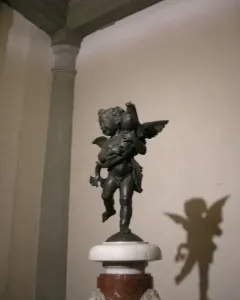 Bronze putto with a dolphin, the winged child poised on one foot atop a small base.