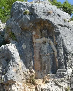 Athena relief carved into a rock face, with a robed figure, a standing column, and carved inscriptions beside it.