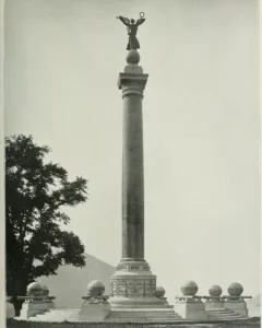 Battle Monument with a tall column topped by a winged female figure holding a wreath aloft, standing on a stepped base with smaller surrounding pedestals.