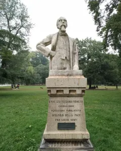 Busto of Ernesto Teodoro Moneta on a tall inscribed pedestal in a grassy park.