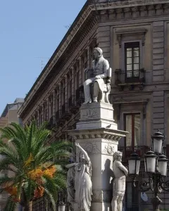 Monument to Vincenzo Bellini with a seated figure atop a marble pedestal and allegorical statues below.