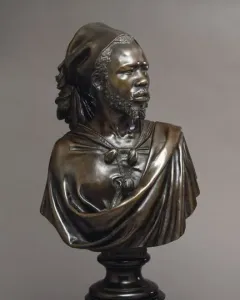 The Nubian Man bronze sculpture shown in three-quarter view on a dark pedestal, with a textured beard, draped garment, and tied head covering.