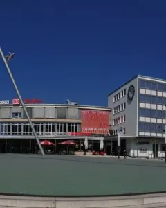 The Man Walking to the Sky sculpture rises on a tilted pole in a plaza in front of the main station buildings.