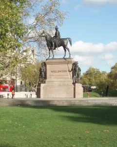 Duke of Wellington statue on a stone pedestal, with smaller figures at the base in a park setting.