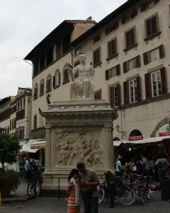 Giovanni delle Bande Nere statue on an ornate pedestal in a busy square with bicycles and pedestrians nearby.