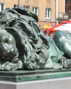 Sleeping Lion bronze sculpture with a green patina, shown lying with its head resting on its front paws.