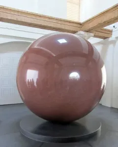 Large Red Sphere on a dark stepped pedestal in a bright room with wooden beams overhead.
