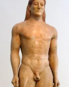 Kroisos Kouros, a front-facing ancient marble statue of a nude young man with braided hair, standing with one leg forward.