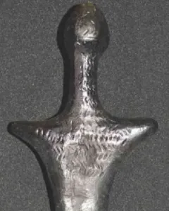 Back view of the Venus of Langenzersdorf sculpture, a dark stylized female figurine with broad shoulders and rounded hips.