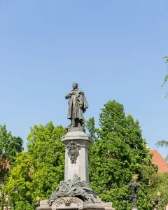 Adam Mickiewicz Monument: a bronze statue of a man in a cloak standing on a tall stone pedestal, with a floral wreath at the base.