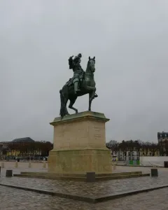 Equestrian Statue of Louis XIV, a green-patinated bronze rider on a rearing horse pointing forward against a blue sky.