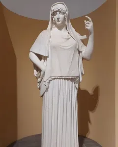 Giustiniani Hestia, a white marble statue of a standing woman in a long pleated robe with a mantle over her head and shoulders.