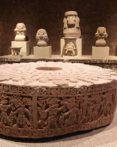 Stone of Motecuhzoma I with detailed carvings, circular frieze figures, and a central depression on top.