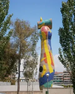 Dona i Ocell sculpture in Barcelona, covered in colorful mosaic tiles with a yellow crescent and ring at the top.