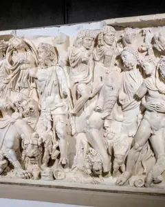 White marble sarcophagus with a densely carved triumphal procession of draped figures and animals in high relief.