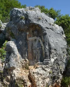 Athena relief carved into a rock face, with a robed figure, a standing column, and carved inscriptions beside it.